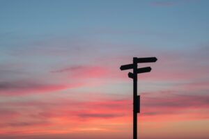a signpost with serval options silhouetted against a sunrise - pink, blue and orange sky
