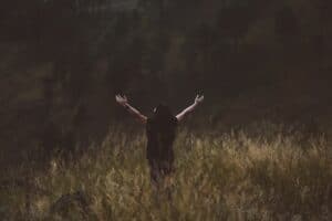 woman praying with arms up in a field