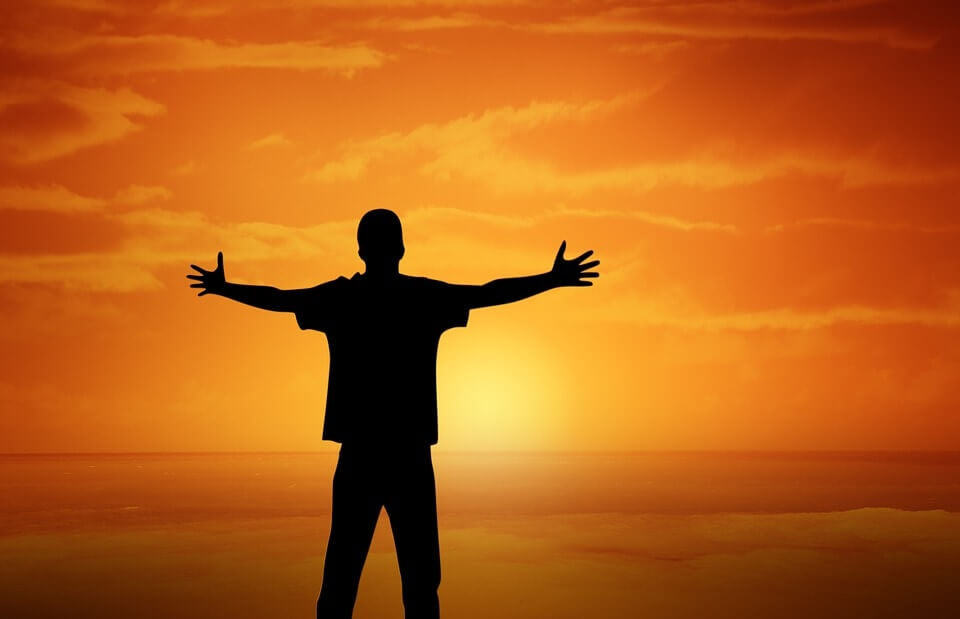 silhouetted man stands in front of sunset